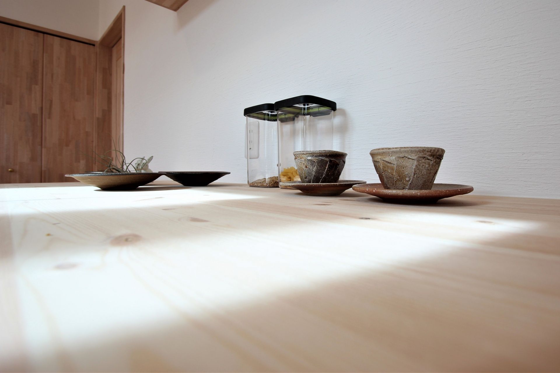 器と植物がひとり分そっと置かれた、木のテーブル
